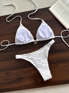 Primer plano de bikini blanco de dos piezas con bordado de flores 3D y dije dorado.