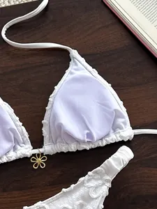 Detalle macro del bikini de encaje blanco con tejido texturizado y dije de flor dorada