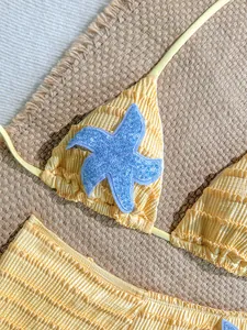 Détail d'un bikini texturé jaune avec une applique d'étoile de mer en paillettes bleues.