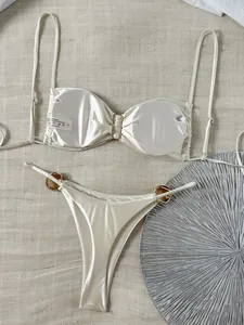 Detailansicht eines cremefarbenen glänzenden Bikinis mit goldenen Metallringen