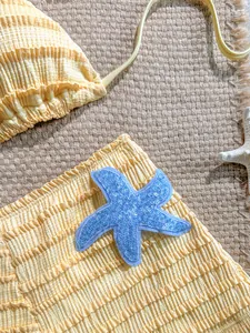 Détail d'un bas de bikini jaune texturé avec un écusson étoile de mer à paillettes