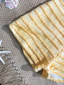 Détail macro montrant le tissu texturé jaune plissé du bas de bikini style shorty.