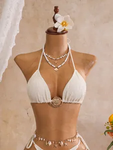 Gedetailleerde weergave van een witte kanten bikiniset met schelpbedels op een mannequin-torso