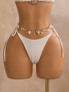 Detail van de gouden buikketting met schelpen op een witte bikini met gaatjes.