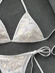 Primer plano de bikini blanco con lentejuelas, apliques florales y tirantes al cuello.
