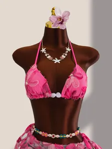 Détail du haut de bikini en maille rose avec broderies florales et paillettes brillantes.