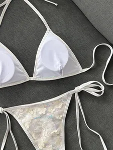 Primer plano de un bikini blanco con apliques florales de lentejuelas y detalles de relleno.