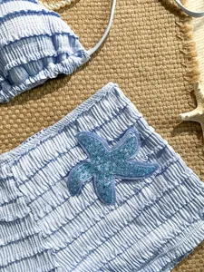 Détail d'un bas de bikini bleu à volants avec un patch étoile de mer en paillettes brillantes.