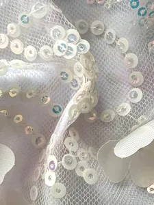 Detalle de lentejuelas blancas bordadas en tela de malla fina para vestidos de fiesta.