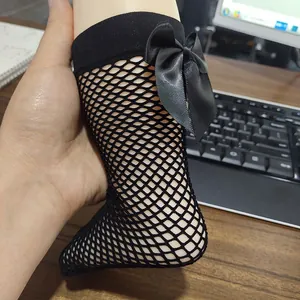 Detailed macro view of girls' black mesh fishnet knee-high socks featuring a satin bow
