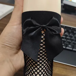 Detail view of girls' black fishnet knee-high socks featuring a large satin bow