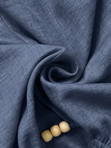 Makroaufnahme der gerippten Stofftextur und der Holzperlen-Details des blauen T-Shirts.