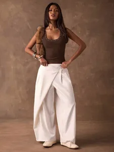 Model trägt ein braunes Y2K ärmelloses Top mit Nieten und eine weiße weite Hose