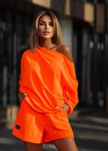 Trendy neon orange off-the-shoulder sweatshirt and shorts set shown on a female model.