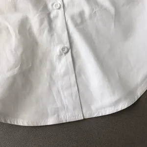 Detail showing the curved hemline and button closure of a white button-down shirt.