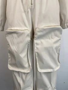 Close-up of beige cargo jumpsuit featuring large zip-up thigh pockets and cinched waist.