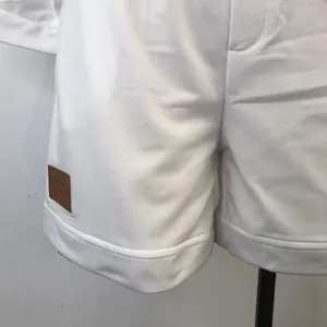 Macro detail shot of white sweatshirt shorts with a decorative brown leather patch detail