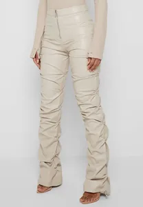 Detalle de pantalones ajustados de cuero sintético beige con fruncidos y bajo acampanado