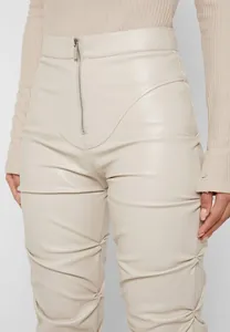 Detalle de pantalones ajustados de cuero sintético con pliegues y cremallera frontal