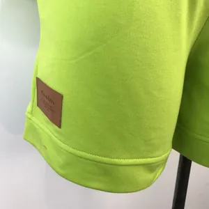 Close-up of lime green sweatshirt hem with brown leather denim patch detail.
