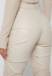Detalle de los pantalones de cuero PU beige con un elegante diseño de pierna fruncida.