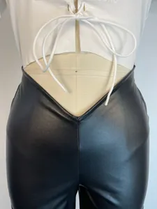 Detailed macro view of black PU leather trousers featuring a low V-waist and straight leg cut