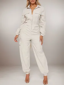 Full body view of a woman wearing a beige utility jumpsuit with front zipper and pockets.
