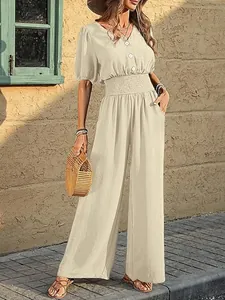 Full-length view of an elegant beige wide-leg jumpsuit with a smocked waist in sunlight