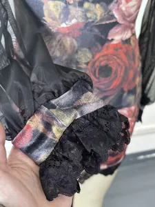 Detail of floral print mesh sleeve with ruffled black lace trim and cuff texture