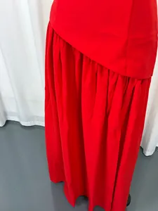 Detail view showing the vibrant red fabric and elegant draped skirt of a formal evening gown.