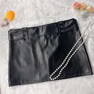 Black PU leather mini skirt featuring silver eyelet details on a white plush background