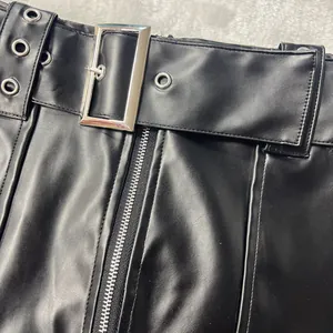 Macro detail view of black PU leather skirt featuring silver metallic belt buckle and central zipper