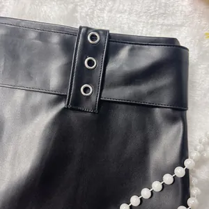 Close-up detail of a sexy black PU leather mini skirt featuring decorative metal grommets