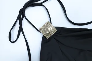 Detailansicht eines schwarzen Neckholder-Kleides mit goldener quadratischer Metallverzierung
