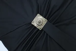 Detailaufnahme eines schwarzen Kleides mit einer gehämmerten quadratischen Goldmetallschnalle.