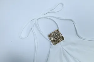 Detailaufnahme eines weißen Neckholder-Kleids mit verzierter goldener Metallschnalle
