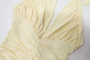 Close-up of pleated details on a light yellow halter neck slim-fit formal dress
