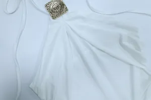 Eine Detailansicht der goldenen Sonnen-Hardware an einem weißen Neckholder-Kleid