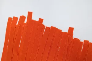 Dettaglio ravvicinato delle frange arancioni vivaci di un abito estivo con scollo