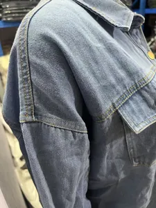 Gros plan de la veste en jean délavé montrant les coutures jaunes et la poche poitrine.