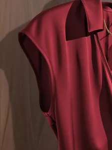 Detail shot of the smooth burgundy satin fabric and shoulder seam of a women's blouse