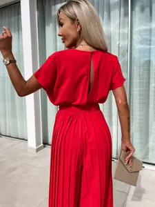 Elegant woman wearing a vibrant red pleated wide-leg jumpsuit with back detail in a patio