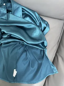 Close-up of teal satin shirt fabric showing luxurious sheen and delicate stitching details