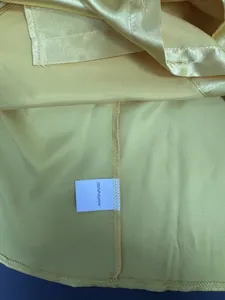 Detalle de camisa de satén amarilla con etiqueta de 100% poliéster y costuras internas