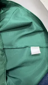Dettaglio ravvicinato del tessuto satinato verde smeraldo 100% poliestere con etichetta interna
