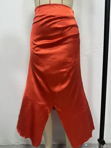 Detail view of an orange high-waisted satin pleated skirt with a front slit.