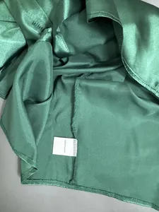 Detailansicht eines grünen Satin-Hemdes mit Stofftextur und 100% Polyester-Etikett
