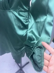 Close-up detail of elastic cuff on an elegant emerald green satin long sleeve dress.