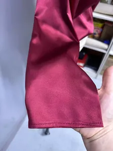 Dettaglio del polsino di una camicia di raso bordeaux che mostra la trama e la cucitura