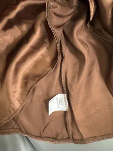 Detalle de blusa de satén marrón con costura interior y etiqueta de 100% poliéster